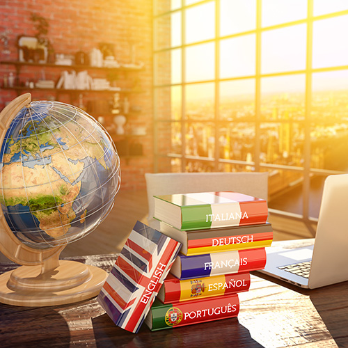 Globus, sechs Wörterbücher und Laptop auf Holztisch in Loft mit Stadtaussicht