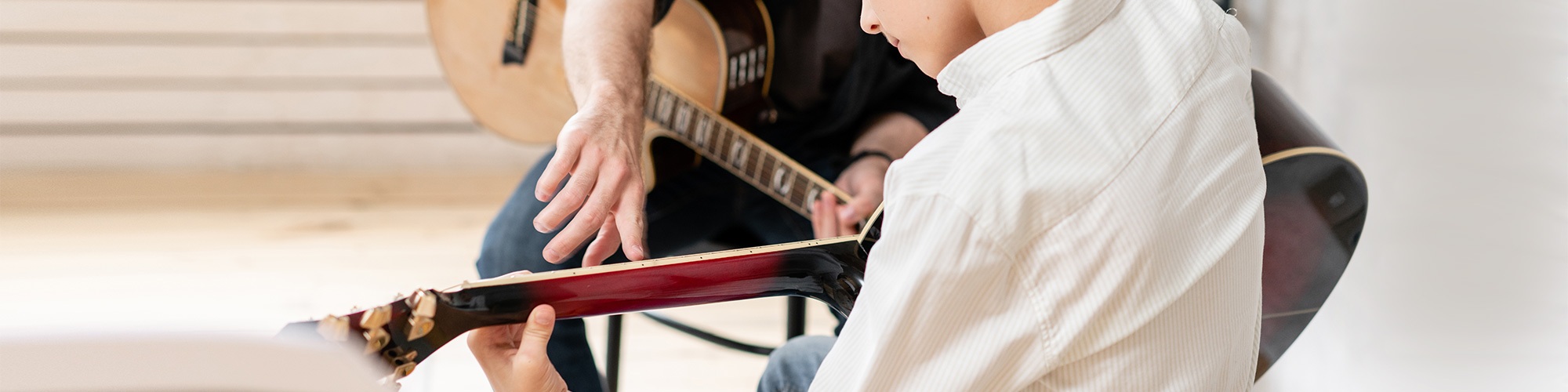 Gitarrenlehrer zeigt bei jugendlichem Schüler auf die Saiten seiner Gitarre